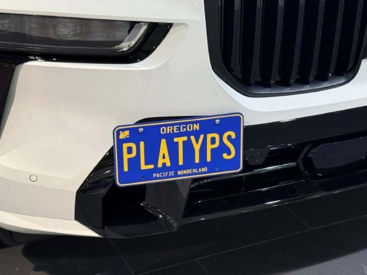 Close up of the Platypus license plate mount on a BMW X7 xDrive40i M Sport bumper showing clear parking sensor (PDC) visibility