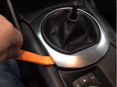carefully prying up the shifter trim ring with a plastic trim panel tool.