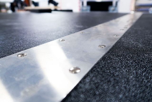 Riveted aluminum edge extrusion running along a black laminate panel