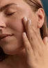 Close-up of a woman gently applying In Essence Barrier Repair Face Oil to her cheek with her fingers.