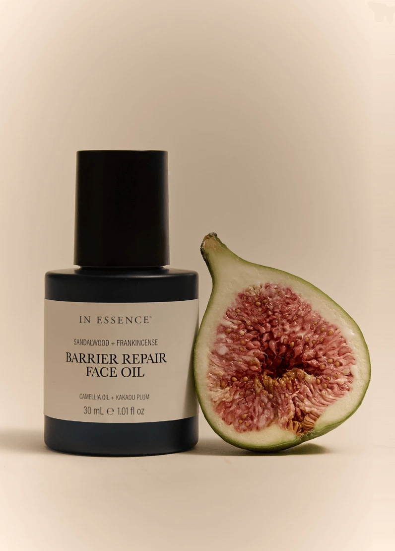 In Essence Barrier Repair Face Oil bottle standing upright beside a fresh fig half, with soft beige background.