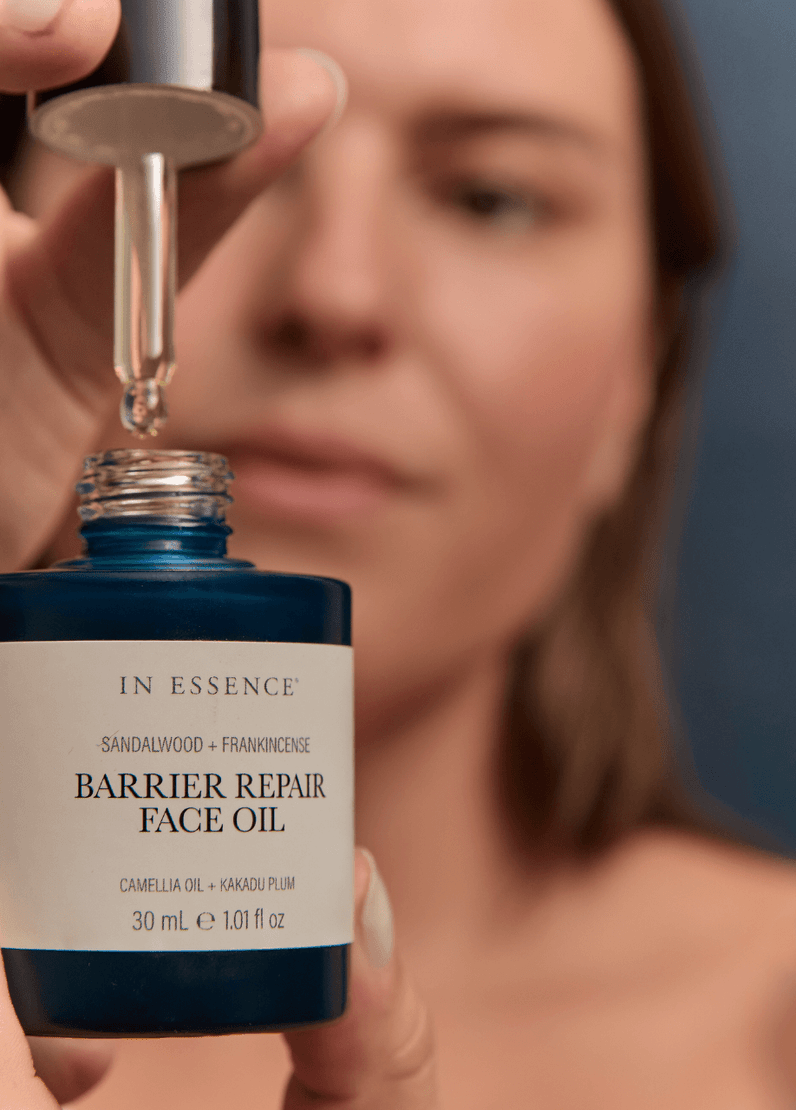 Woman holding open In Essence Barrier Repair Face Oil bottle with dropper, preparing to apply the product.