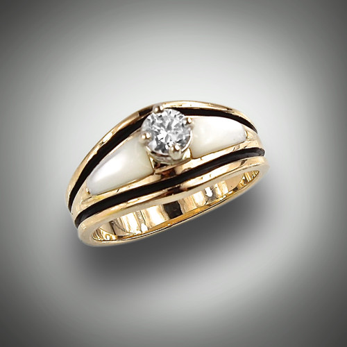 R 709 ring has a traditional shape and holds a solitaire round Diamond in the center. Mother of Pearl is inlaid to either side, glowing with Opalescence. A black oxidized line frames all and is set in 14kt yellow gold.