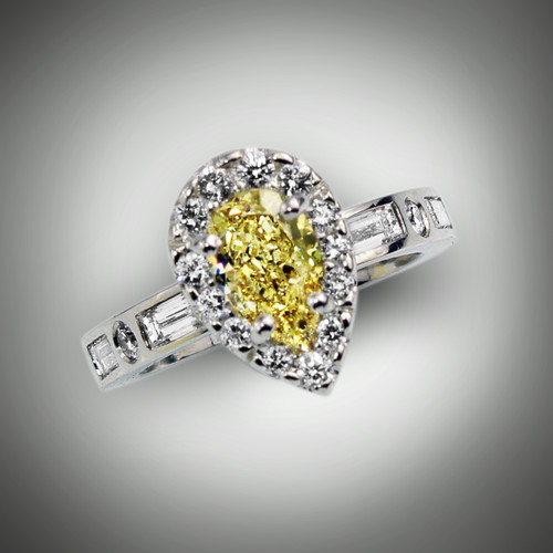 R 1223 this women’s ring has a 1.05 ct fancy deep yellow color and SI1 clarity pear shape diamond.   The center stone is surrounded by a halo of  F/VS pave` round diamonds of 18 points and the shank has 3.4 points F/VS round diamonds and 0.32 points baguettes set in 18kt white gold.   