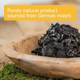 Dark moor mud paste showing its moist, earthy texture, stirred with a teaspoon