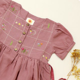 a hand-embroidered yoke with miniature motifs, wood button details, and short gathered sleeves.