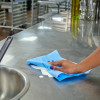 Hand using a Sellars Clean Task blue quarterfold foodservice wiper to clean food prep surface in a commercial kitchen environment