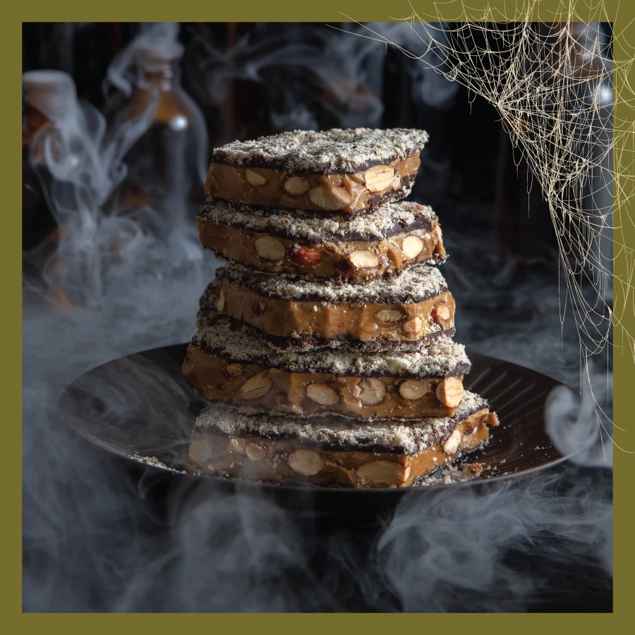 Traditional Almond Toffee in Dark Chocolate on a Plate with Smoke and Bottles