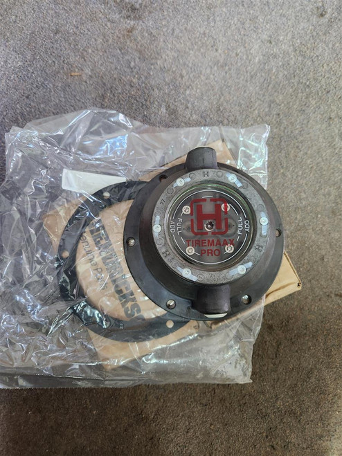 Close-up of Hendrickson VS-32056-1 Tiremaax Pro HP oil hub cap resting on clear packaging and cardboard box, showing red Tiremaax Pro logo at center and six-bolt mounting flange.