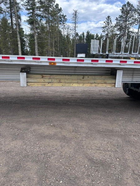 Pair of aluminum trailer dunnage carriers installed along a flatbed trailer with lumber