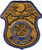 A shield-shaped embroidered patch features an eagle above a circular emblem, surrounded by the text "Department of the Army, CID Agent," set against a yellow and blue background.