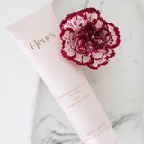 A pink cleansing cream tube with floral design, accompanied by a red and white carnation flower, on a marble surface.