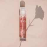 A clear bottle of body exfoliating mist with a pink tint, labeled "Fleur's," casting a shadow of a flower on a beige background.