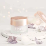 A jar of Fleur's Golden Cream on a speckled surface, surrounded by delicate flower petals and soft lighting.
