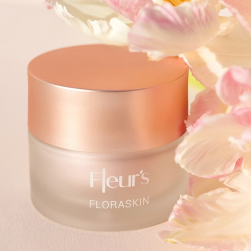 A glass jar of Fleur's Floraskin cream with a rose gold lid, surrounded by delicate flowers 