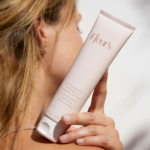A person holds a tube of Fleur's Floral Smoothie Cleansing Foam Cream, showcasing the product against a light background.