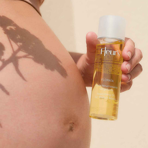 A close-up of a hand holding a bottle of nourishing oil for stretch marks, with a shadow of a plant on a pregnant bare belly. A close-up of a hand holding a bottle of nourishing oil for stretch marks, with a shadow of a plant on a pregnant bare belly.