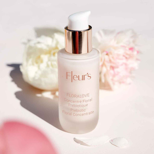A frosted glass bottle of Fleur's Floralove prebiotic floral concentrate, with a white pump top, surrounded by soft floral elements.
