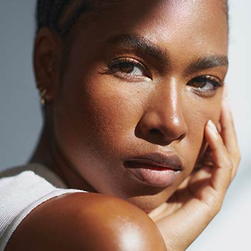 A close-up portrait of a person with smooth skin, resting their chin on their hand, with soft lighting highlighting their features.