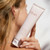 A person holds a tube of Fleur's Floral Smoothie Cleansing Foam Cream, showcasing the product against a light background.
