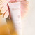 A tube of Fleur's Floraïa Hydra-Gentle Cream is placed against a soft pink flower backdrop.