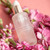 A frosted glass bottle of hydrating gel surrounded by pink flowers on a soft pink background.