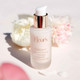 A frosted glass bottle of Fleur's Floralove prebiotic floral concentrate, with a white pump top, surrounded by soft floral elements.