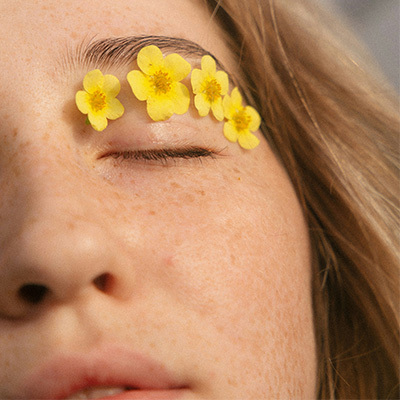 Yellow Flowers lay along a woman's eye lid with her eye's closed.