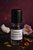 Black-capped 5 ml rollerball labeled “Versace Crystal Noir Fragrance Oil (W)” on a deep burgundy background with soft bokeh, dark surface, black peppercorns, ginger slice, cardamom pods, coconut piece, gardenia and peony blooms, orange blossom, sandalwood curls, and an amber resin bead. Black-capped 5 ml rollerball labeled “Versace Crystal Noir Fragrance Oil (W)” on a deep burgundy background with soft bokeh, dark surface, black peppercorns, ginger slice, cardamom pods, coconut piece, gardenia and peony blooms, orange blossom, sandalwood curls, and an amber resin bead.
