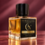 Cherry After Dark 50 mL Extrait de Parfum by Alchemy & Aura Parfums, featuring a clear glass bottle, amber-colored perfume, black cap, and black-and-gold label against a burgundy background.