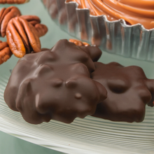 Lammes Candies Dark Chocolate Longhorns are elegantly arranged on a glass plate, showcasing their smooth dark chocolate coating over crunchy pecans and creamy caramel.