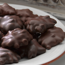 Lammes Candies Dark Chocolate Longhorns are piled on a white plate, showcasing their smooth dark chocolate coating over crunchy pecans and creamy caramel.