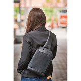 A sleek black and grey sling backpack is worn across the back of a person in a city setting.