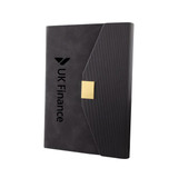 A sleek black notebook with a textured cover and a gold clasp, featuring a logo on the front.