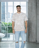 A man stands wearing a bleach-out dyed T-shirt in neutral tones, paired with ripped blue jeans.