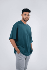 A unisex oversize easyfit tee in teal worn with grey sweatpants, featuring a logo on the tee.