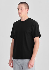 A black men's box tee displayed on a model, featuring a relaxed fit and short sleeves.