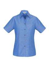 A women's short sleeve button-up shirt in light blue chambray fabric, featuring a single chest pocket and a branded logo.