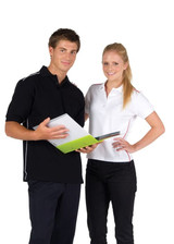 A man in a black polo shirt and a woman in a white polo shirt stand together, holding a folder. Both shirts feature contrasting piping.