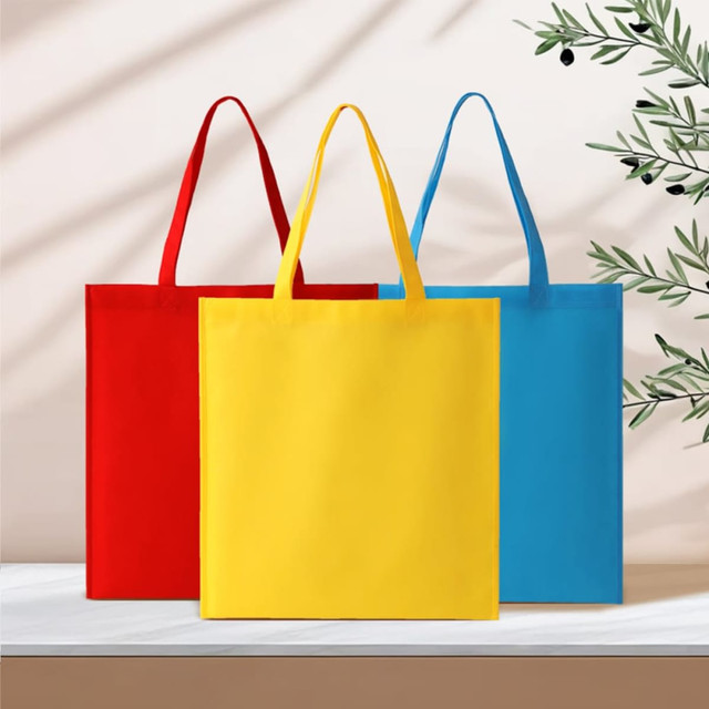 A set of three tote bags in red, yellow, and blue with handles, displayed on a surface with a minimal background.