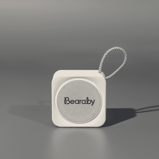 A compact white portable Bluetooth speaker with a loop for attachment. Features a logo on the front.