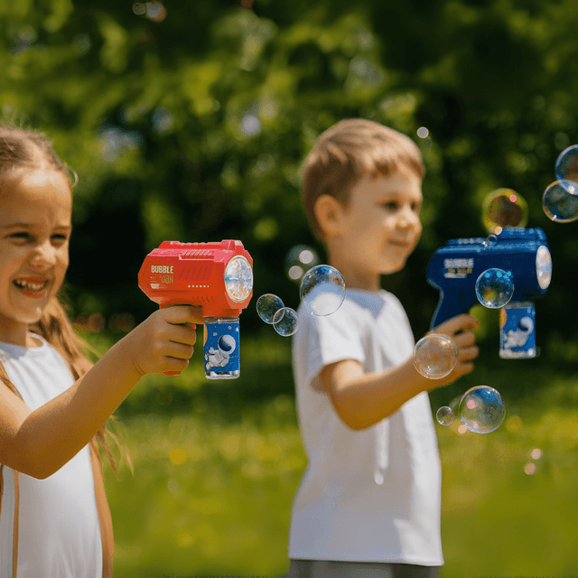 A red and a blue bubble gun are held by children, creating bubbles against a blurred green backdrop.