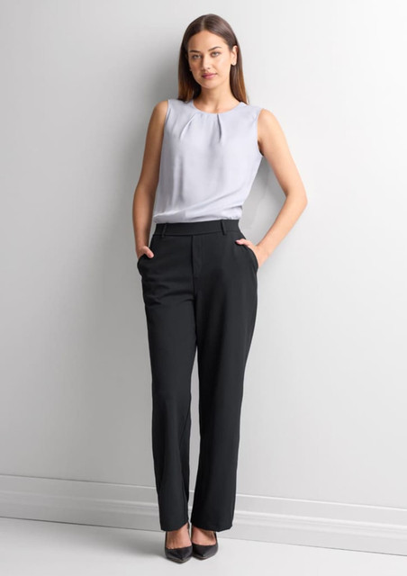 A woman wearing black soft stretch pants paired with a light grey top, standing against a plain background.