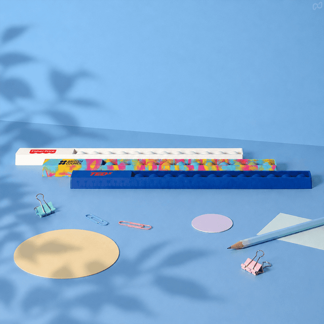 A 30cm popper ruler in blue with a colourful design, surrounded by stationery items like paperclips and circular paper.
