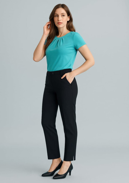 A woman wearing a turquoise top and black slim leg pants, standing against a light grey backdrop. The pants feature pockets and a logo.