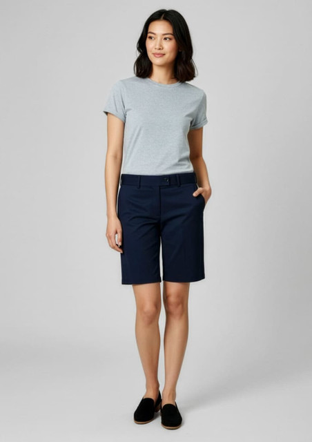 A woman wearing navy shorts and a grey t-shirt stands against a neutral background. The shorts have a waistband and pockets.