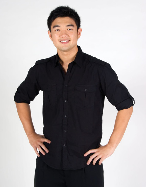 A man wearing a black long sleeve button-up shirt with two chest pockets and rolled-up sleeves.