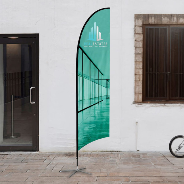 A medium feather flag kit with a teal design, featuring a logo, set up outdoors.