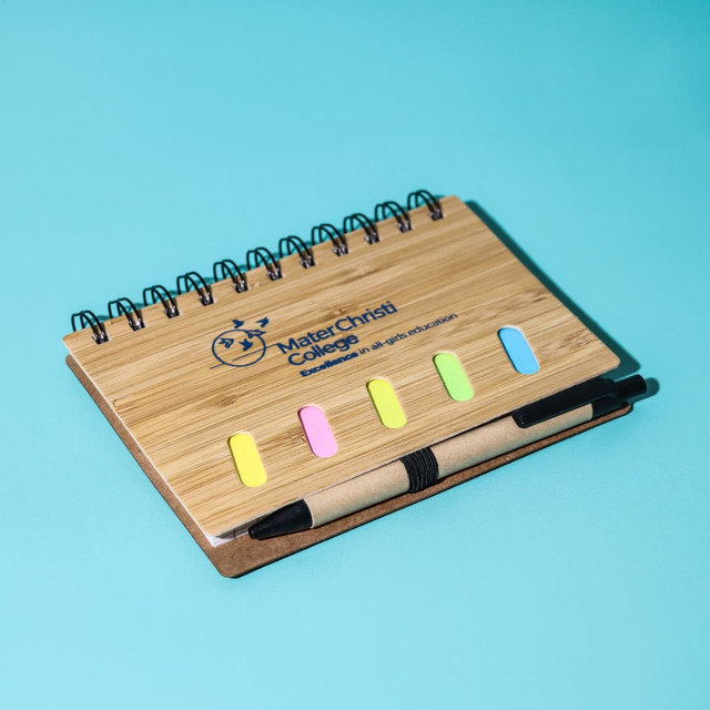 A bamboo notebook with a pen, featuring a spiral binding and multicoloured sticky tabs on the cover.