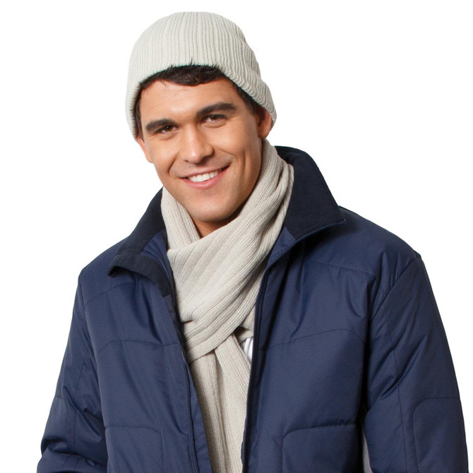 A man wearing a light grey cable knit beanie and a matching scarf, paired with a navy jacket. The image has a logo present.